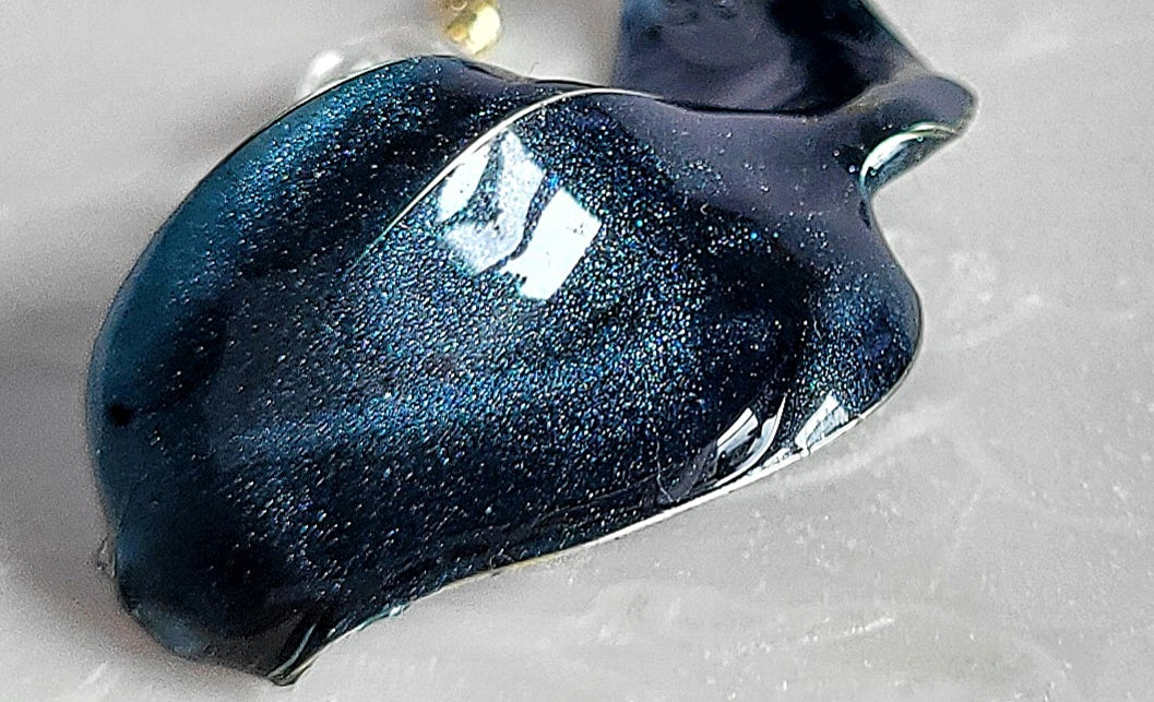 Close-up of a blue glitteryHandcrafted long gold wire earrings with navy blue starry cat eye resin flowers, zirconia starburst crystal studs, waterdrop crystals, and raindrop dangles.