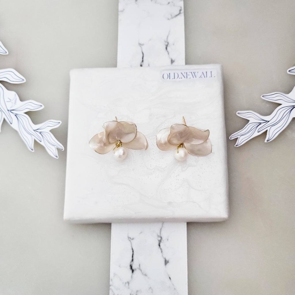 Handcrafted white resin orchid drop earrings featuring layered petals and elegant dangling natural freshwater pearls, displayed on a square marble textured surface.