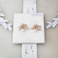Handcrafted white resin orchid drop earrings featuring layered petals and elegant dangling natural freshwater pearls, displayed on a square marble textured surface.