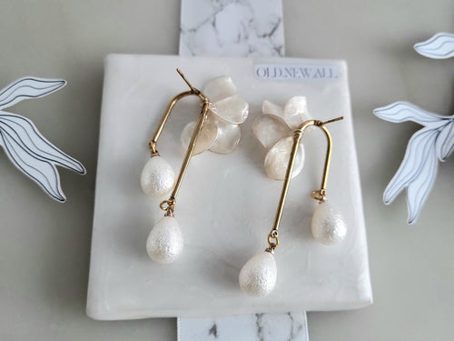 Handcrafted white resin orchid drop earrings featuring powder effect layered petals and dangling waterdrop faux pearl charms, styled for an elegant wedding look.