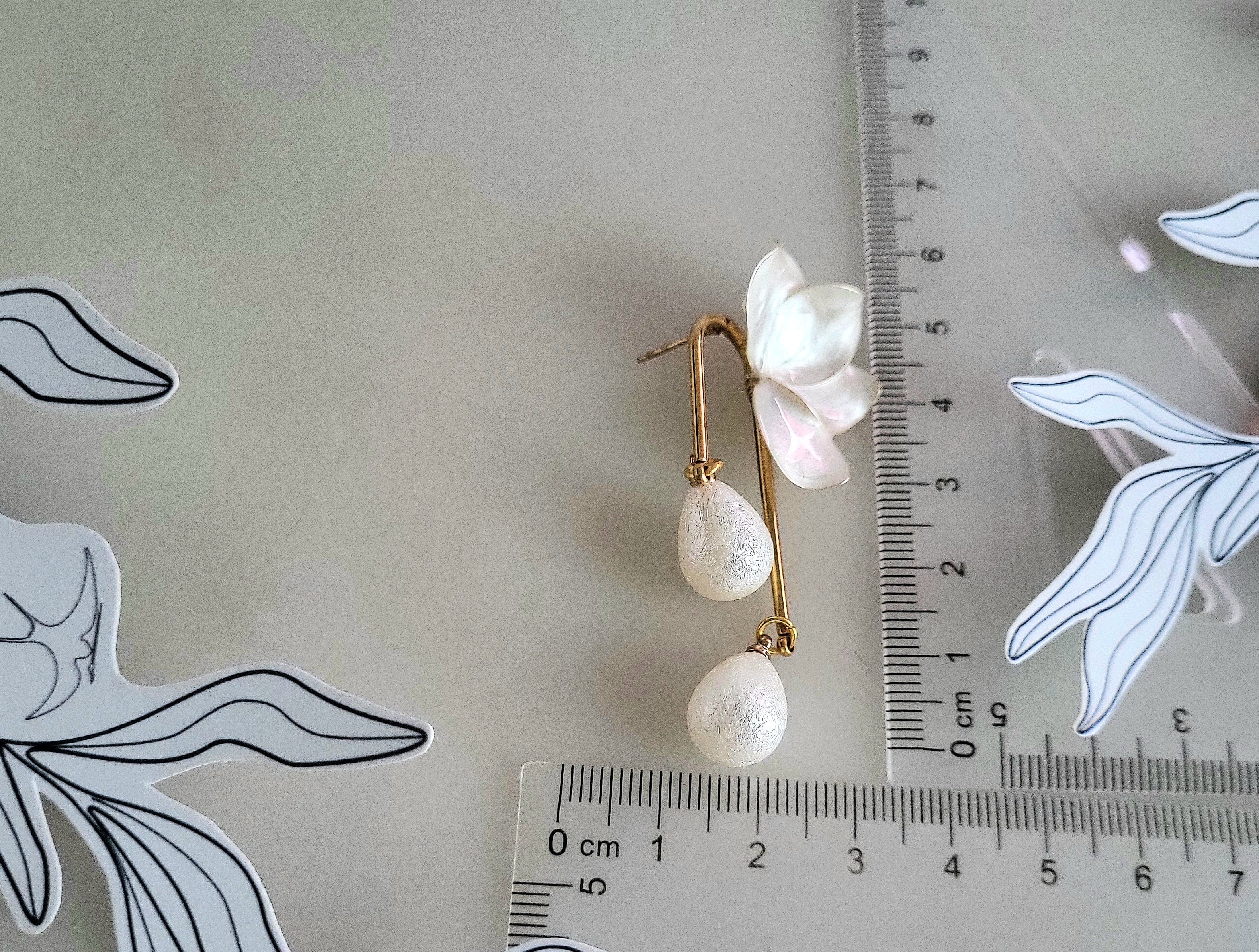 Handcrafted white resin orchid drop earrings featuring powder effect layered petals and dangling waterdrop faux pearl charms, styled for an elegant wedding look.