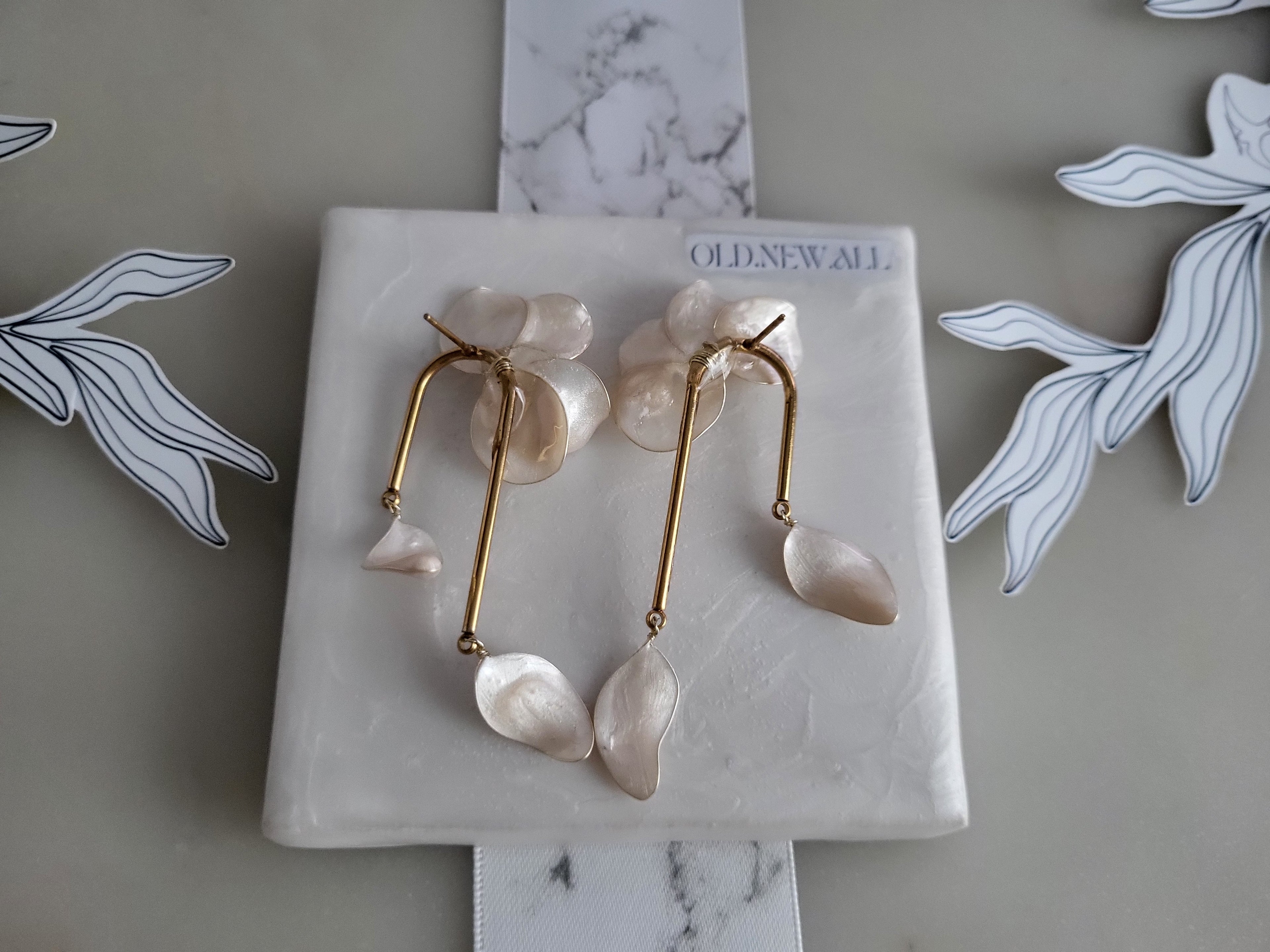 Large handcrafted flower earrings with opaque pearlescent petals and bridal aesthetic charms, displayed on a natural wood surface.