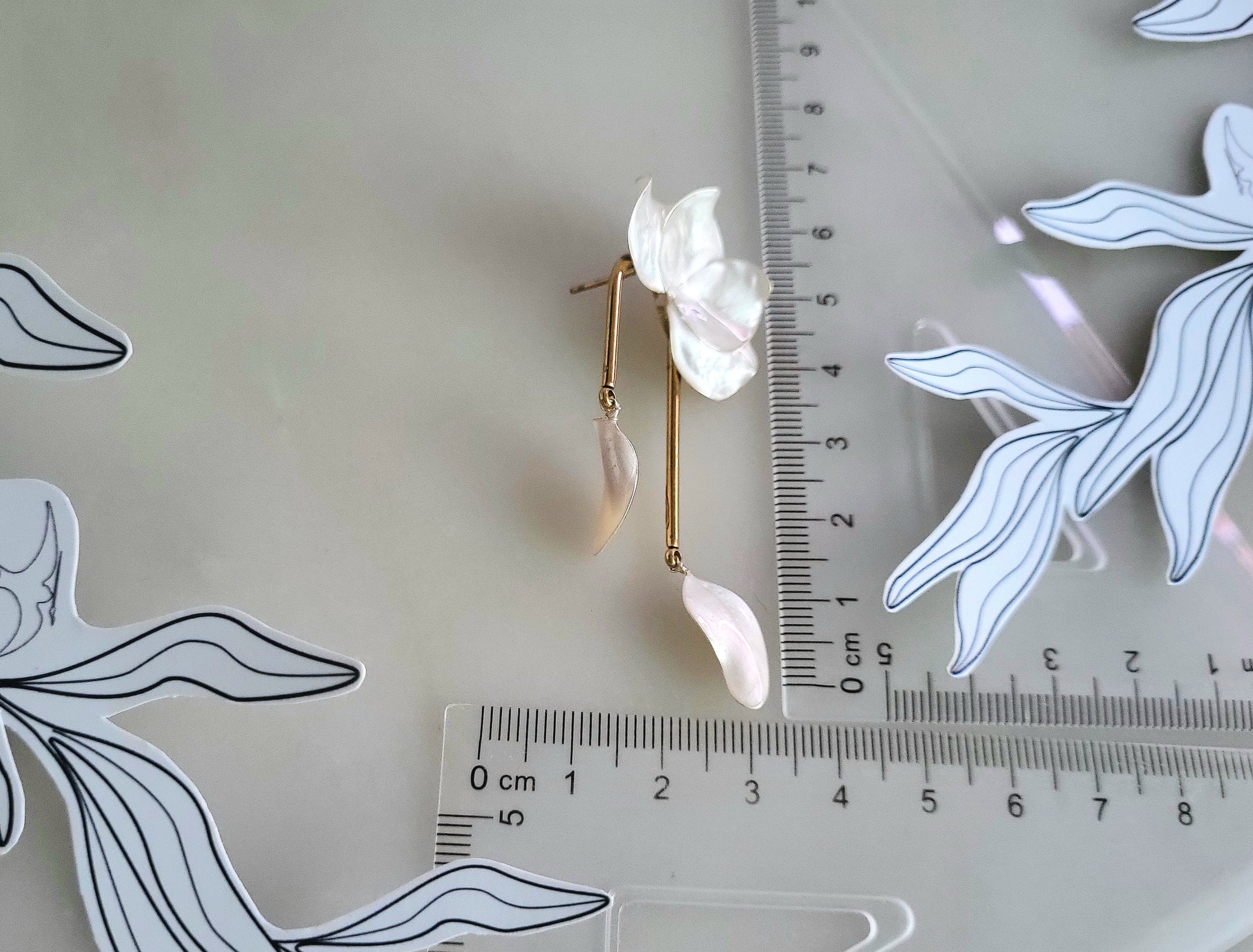 Large handcrafted flower earrings with opaque pearlescent petals and bridal aesthetic charms, displayed on a natural wood surface.