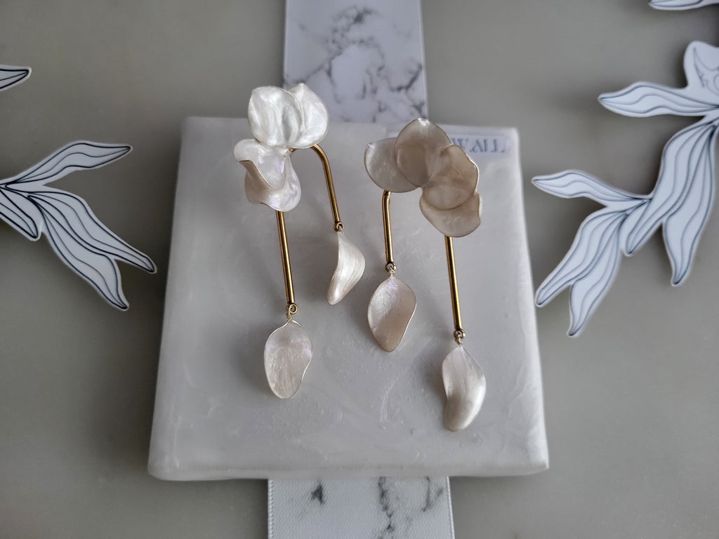 Large handcrafted flower earrings with opaque pearlescent petals and bridal aesthetic charms, displayed on a natural wood surface.