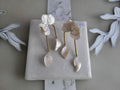 Large handcrafted flower earrings with opaque pearlescent petals and bridal aesthetic charms, displayed on a natural wood surface.