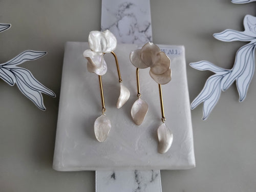 Large handcrafted flower earrings with opaque pearlescent petals and bridal aesthetic charms, displayed on a natural wood surface.