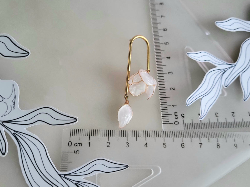 Handcrafted golden arch mismatched tulip earrings featuring a translucent white resin flower charm and a dangling motherofpearl petal drop with ruler