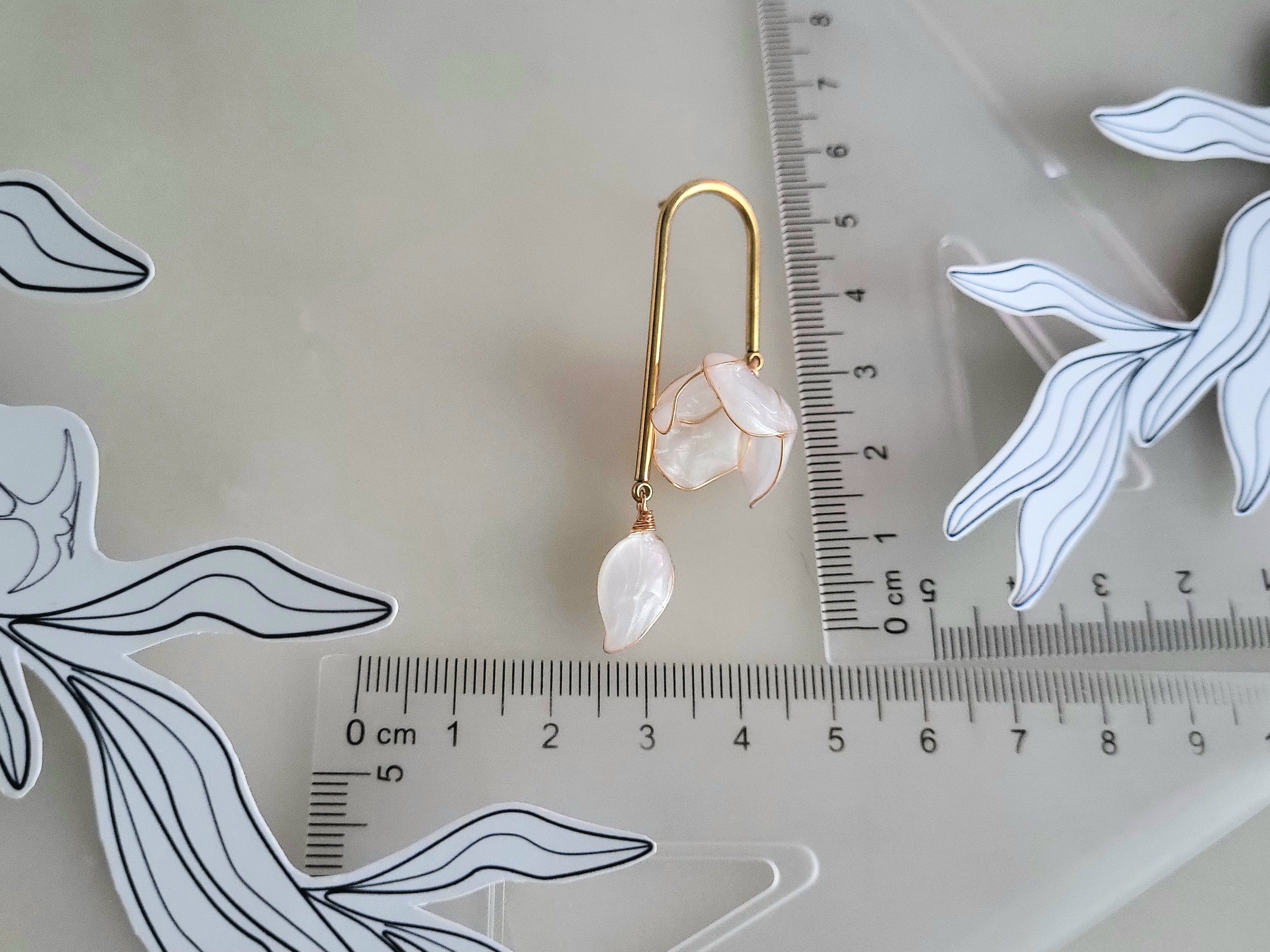 Handcrafted golden arch mismatched tulip earrings featuring a translucent white resin flower charm and a dangling motherofpearl petal drop with ruler
