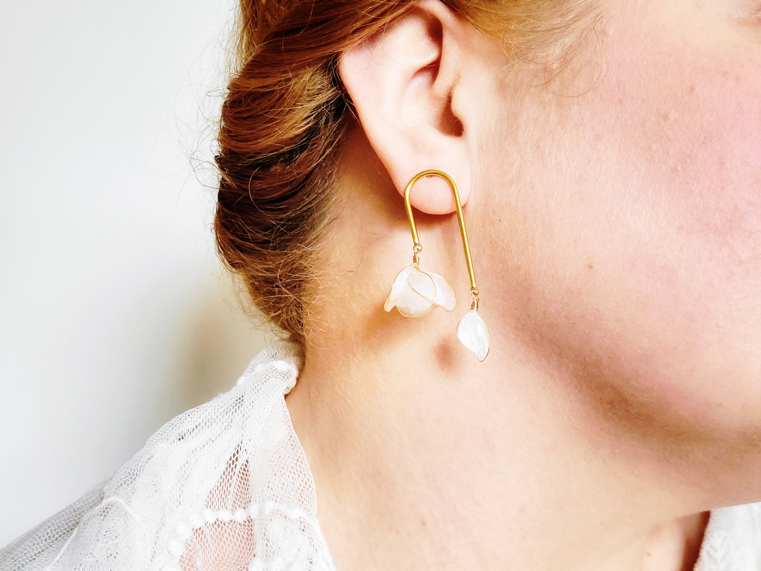 Handcrafted golden arch mismatched tulip earrings featuring a translucent white resin flower charm and a dangling motherofpearl petal drop.