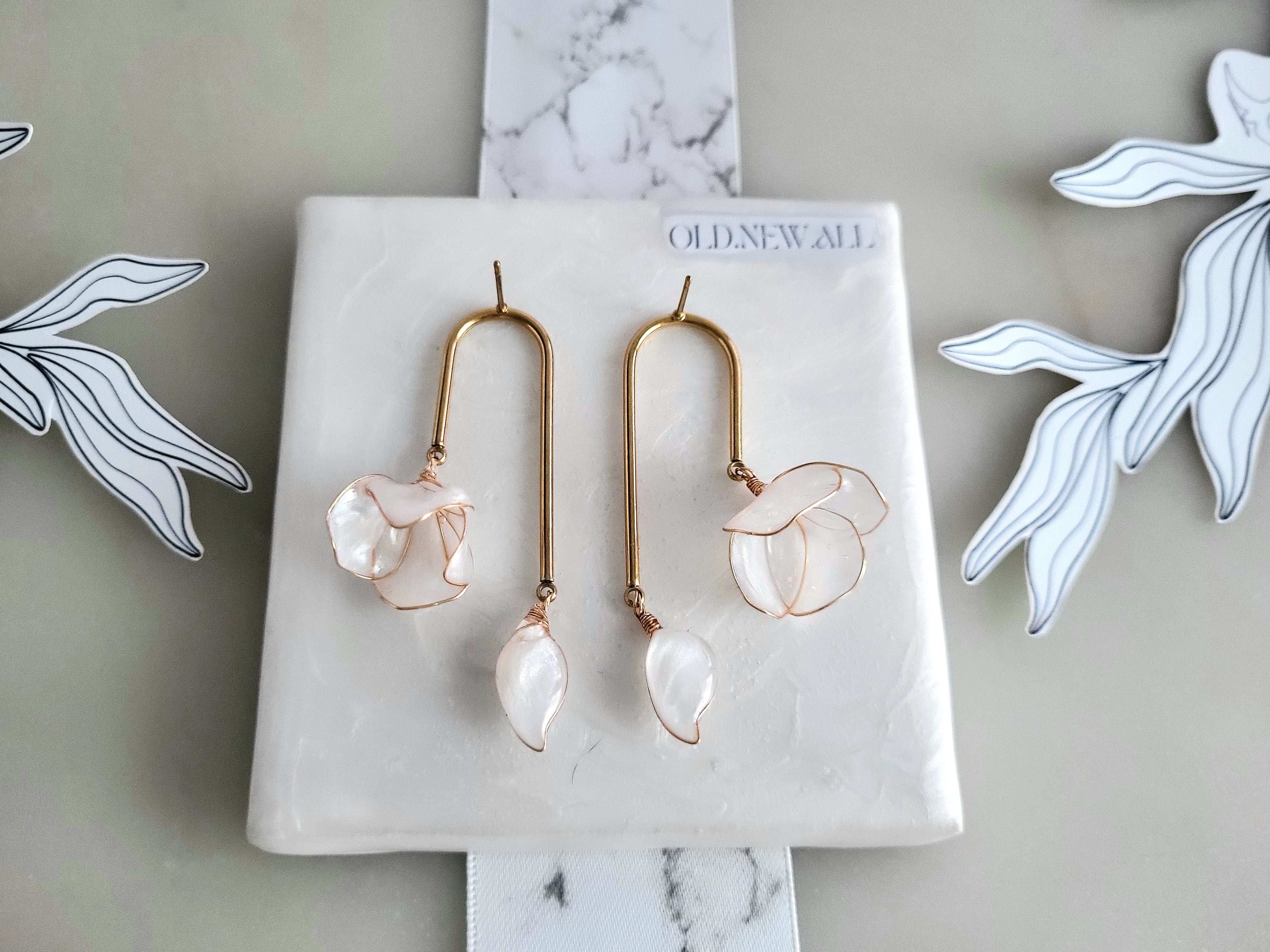 Handcrafted golden arch mismatched tulip earrings featuring a translucent white resin flower charm and a dangling motherofpearl petal drop.