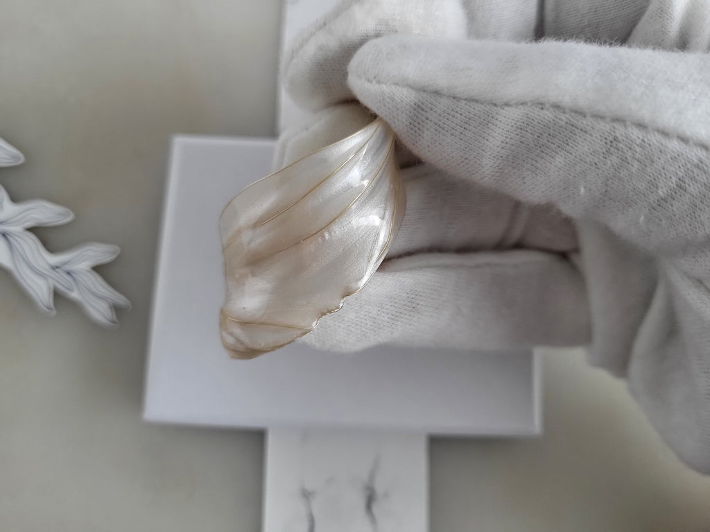 Close-up of Handcrafted white pearl studs with an embedded gold heart, featuring a delicate chain with a twisted wire white resin petal drop design.