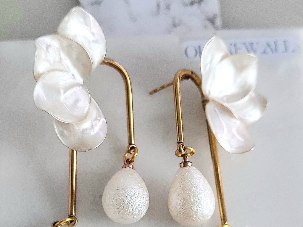 Handcrafted white resin orchid drop earrings featuring powder effect layered petals and dangling waterdrop faux pearl charms, styled for an elegant wedding look.