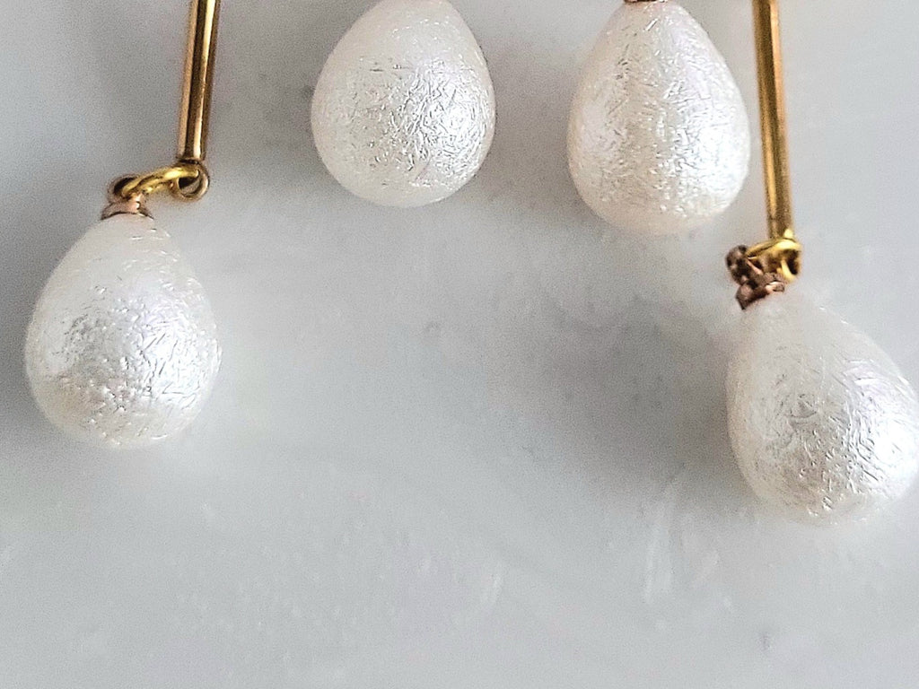 Handcrafted white resin orchid drop earrings featuring powder effect layered petals and dangling waterdrop faux pearl charms, styled for an elegant wedding look.