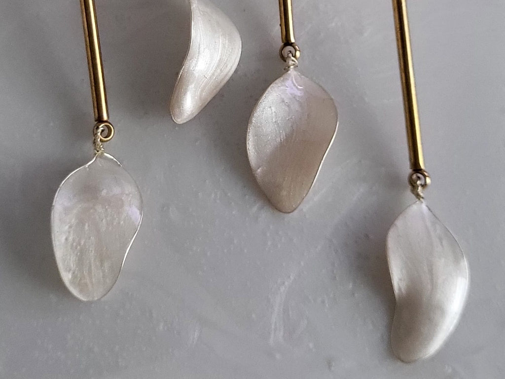 Large handcrafted flower earrings with opaque pearlescent petals and bridal aesthetic charms, displayed on a natural wood surface.
