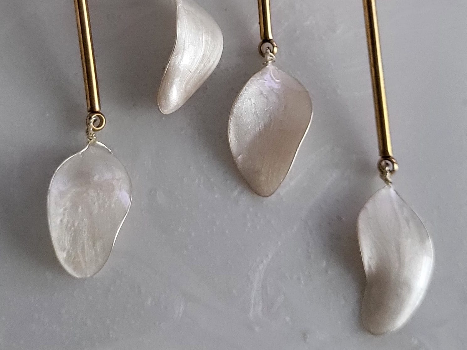 Large handcrafted flower earrings with opaque pearlescent petals and bridal aesthetic charms, displayed on a natural wood surface.