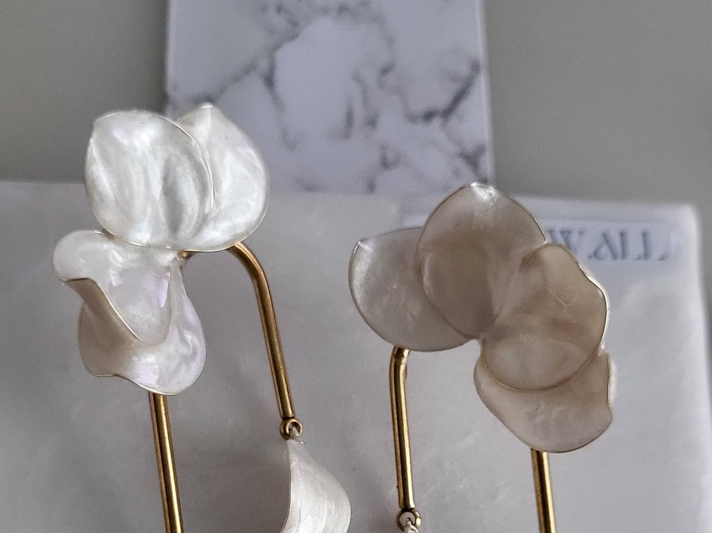 Large handcrafted flower earrings with opaque pearlescent petals and bridal aesthetic charms, displayed on a natural wood surface.