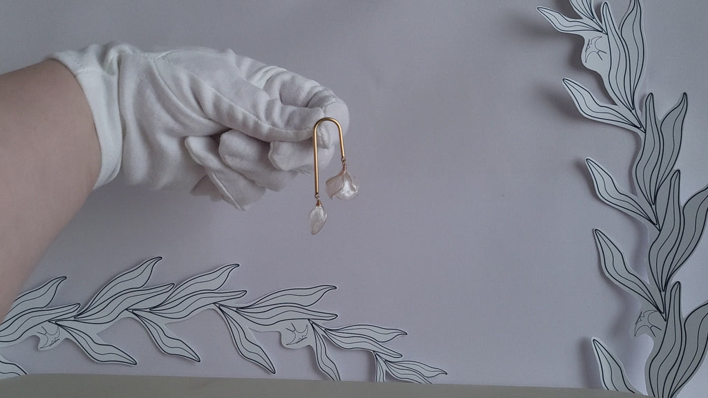 Handcrafted golden arch mismatched tulip earrings featuring a translucent white resin flower charm and a dangling motherofpearl petal drop.