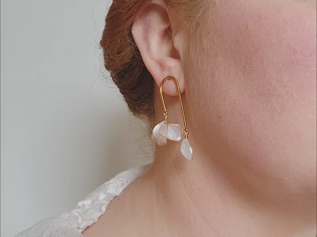 Handcrafted golden arch mismatched tulip earrings featuring a translucent white resin flower charm and a dangling motherofpearl petal drop.
